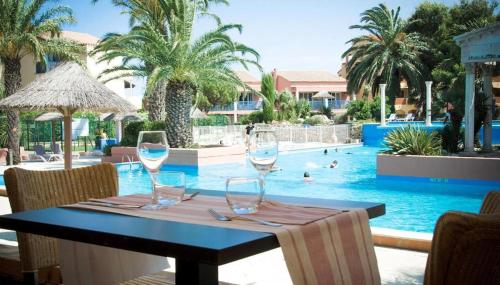 a table with wine glasses in front of a swimming pool at Appartement Spacieux T2, Confortable Malibu Village, Canet-en-Roussillon in Canet-en-Roussillon