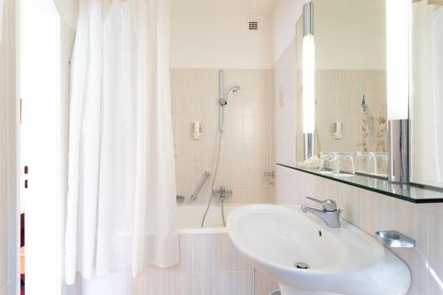 a white bathroom with a sink and a shower at Romantik Hotel zur Sonne in Badenweiler
