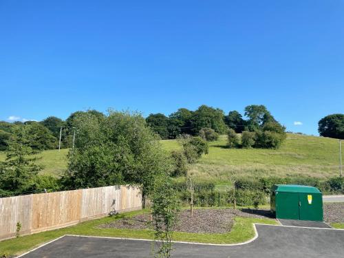 a parking lot with a fence and a green dumpster at Brand-New, 2 Private Bedrooms Available, Stunning Views, Stoke Hospital, Alton Towers, Keele University, Trentham Gardens, Free Parking & Wi-Fi in Silverdale