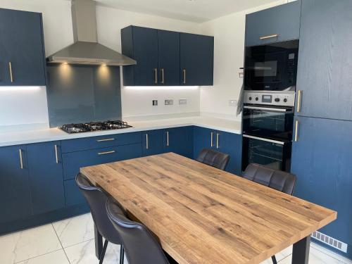 a kitchen with blue cabinets and a wooden table at Brand-New, 2 Private Bedrooms Available, Stunning Views, Stoke Hospital, Alton Towers, Keele University, Trentham Gardens, Free Parking & Wi-Fi in Silverdale