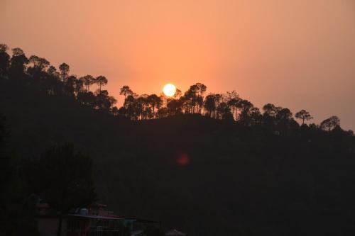 a sunset over a hill with trees on it at The Blissful Escapes !!! in Dharampur