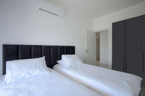 a bedroom with two white beds and a black headboard at Most perfect 4-BDR with jacuzzi BY MadrigalRentals in Qiryat Ata