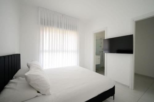 a white bed with white pillows and a window at Most perfect 4-BDR with jacuzzi BY MadrigalRentals in Qiryat Ata