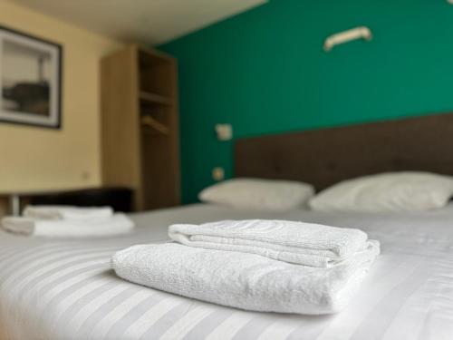 two towels on a bed with a green wall at Family Hôtel in Wavre