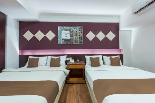 two beds in a room with a purple wall at Hotel Grand Orchard in Gua Sai