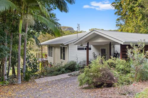 a small white house with a porch and trees at Quiet Ninderry Cottage with Peaceful Rural Outlook in Ninderry