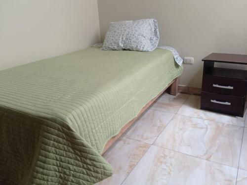 een bed met een groene deken en een nachtkastje bij Oceánica Lodge in Ilo