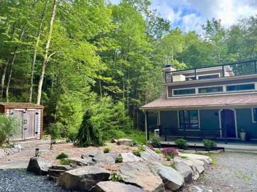 a house in the woods with rocks in the yard at Tuthill Tree House - Secluded Mountain Cabin with Roof Deck in Shohola