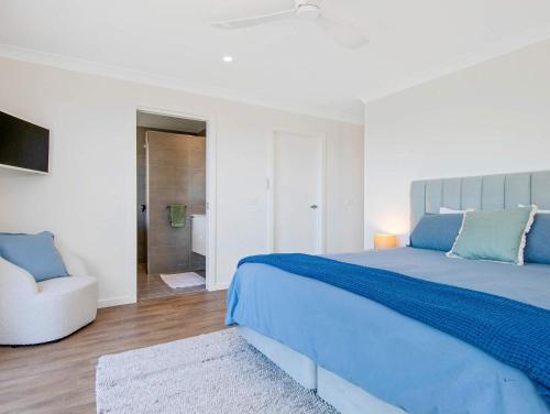 a white bedroom with a blue bed and a chair at Garden Bay Coastal Retreat in Malua Bay