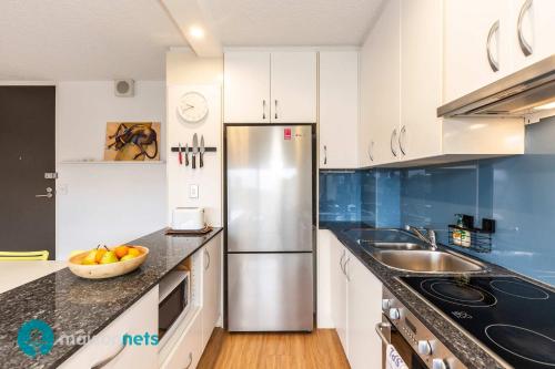 a kitchen with white cabinets and a stainless steel refrigerator at Light Filled 1BR Retreat with Car Park & Pool in Sydney