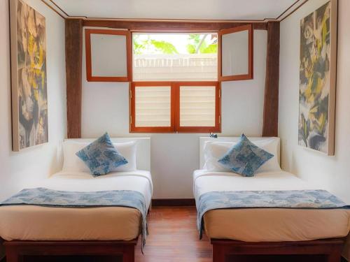 two twin beds in a room with a window at My BanLao Hotel in Luang Prabang