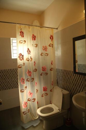 a bathroom with a toilet and a shower curtain with flowers at Beachside Bliss - Villa 32 in Kilpettai