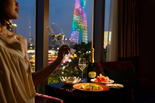 a woman drinking a glass of wine in front of a window at Hotel Indigo Guangzhou Haixinsha by IHG - Free Shuttle Bus to Canton Fair Complex during Canton Fair period in Guangzhou