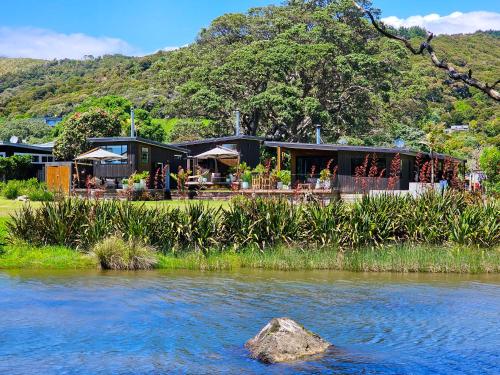 a building next to a river with a rock in the foreground at Adventurer's Chest - Pohutukawa in Hotwater Beach