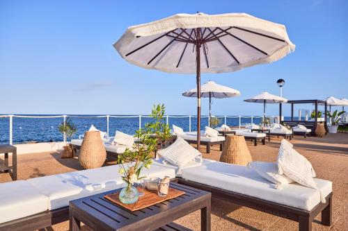 a patio with white couches and an umbrella and the ocean at AluaSoul Menorca - Adults Only in S'Algar