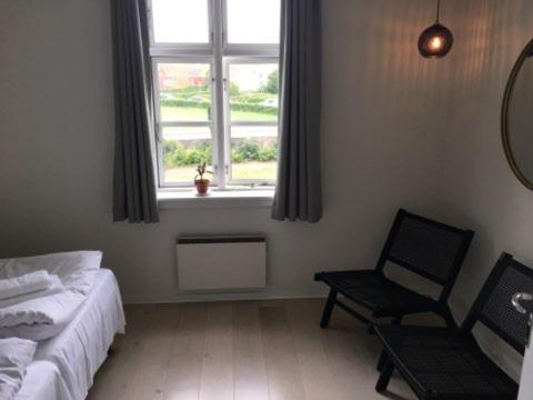 a bedroom with a bed and a chair and a window at Villa Koch X Pension Koch in Gudhjem