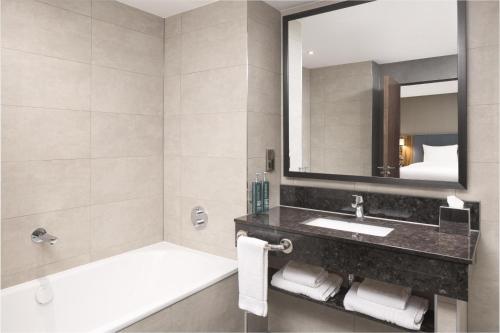 a bathroom with a tub and a sink and a mirror at Hilton Garden Inn London Heathrow Terminal 2 and 3 in Hillingdon
