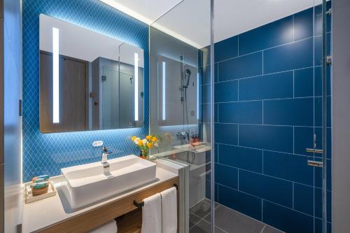 a bathroom with a sink and a mirror and blue tiles at Orange Hotel, Longhu Paradise Walk, Daxing Biomedical Base, Beijing in Beijing