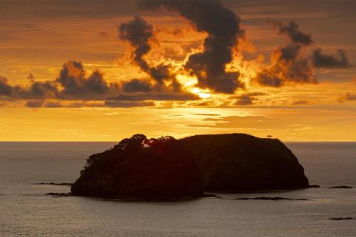 a small island in the ocean with a sunset at Waldorf Astoria Costa Rica Punta Cacique in Playa Hermosa
