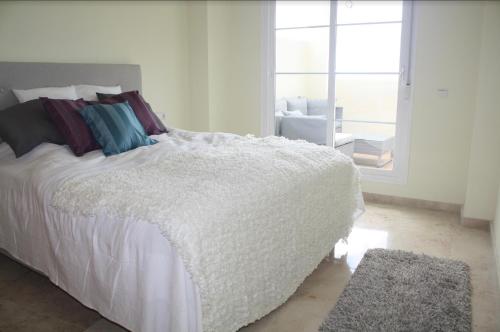 sypialnia z białym łóżkiem z poduszkami i oknem w obiekcie Benalmadena Home w mieście Benalmádena