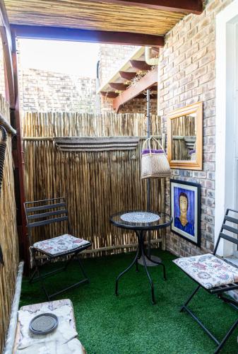 a patio with two chairs and a table and a table and benches at Earthbound Guest House in Oudtshoorn