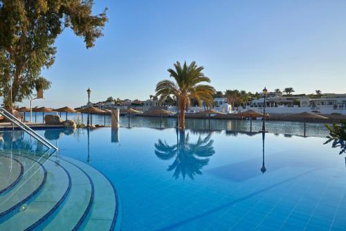 a large swimming pool with a palm tree and houses at Hotel Sultan Bey Resort in Hurghada