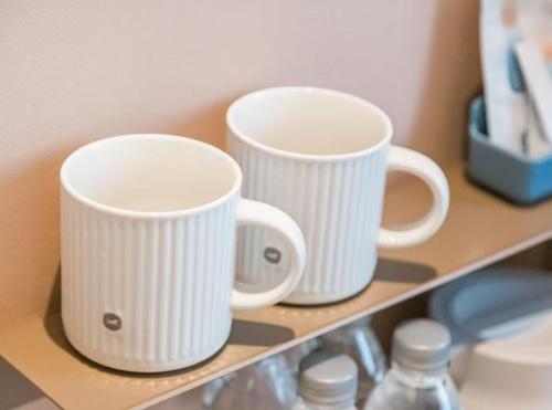 two white coffee mugs sitting on a shelf at Hanting Hotel Beijing Shangdi Zhongguancun Software Park in Beijing
