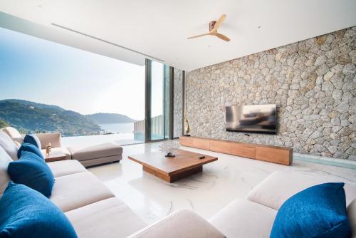 a living room with white furniture and a stone wall at Sea Theatre Kata by ROI in Ban Nong Chaeng