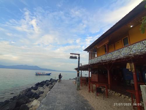 a man standing next to a building next to the water at Three Ken Homestay & Cafe in Manado