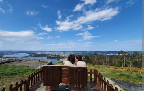 two people sitting on a bench looking out over a river at Real 49 camiño Santiago in Neda