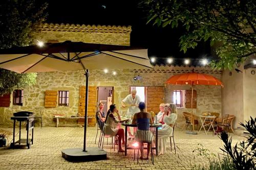 a group of people sitting at a table under an umbrella at Maison des Vignes Swimming pool and charm in Lauris in Lauris