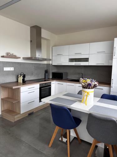 a kitchen with white cabinets and a table with blue chairs at Gamma Apartmanok és Jakuzzi in Miskolctapolca
