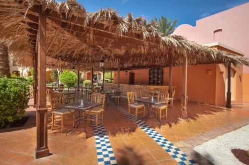 a restaurant with tables and chairs under a straw umbrella at JAZ Makadi Saraya Resort in Hurghada