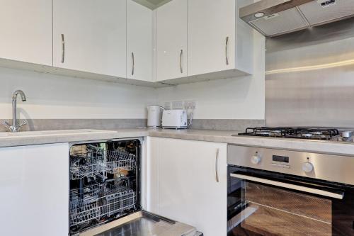 a kitchen with white cabinets and an open dishwasher at Luxury and cosy 2 bed entire house in Essex 20 mins from beach in Colchester
