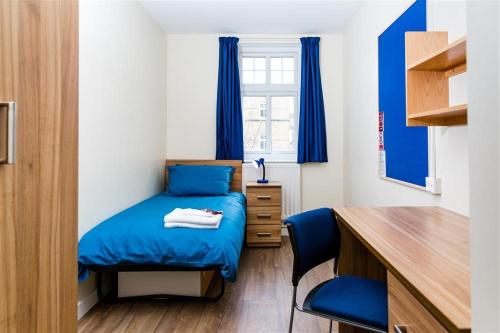 a small bedroom with a blue bed and a desk at Alexander Fleming House, London in London