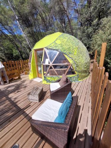 a tent on a wooden deck with a wicker chair and a wicker at Logements insolites du Domaine de la Tuilière in Carnoules