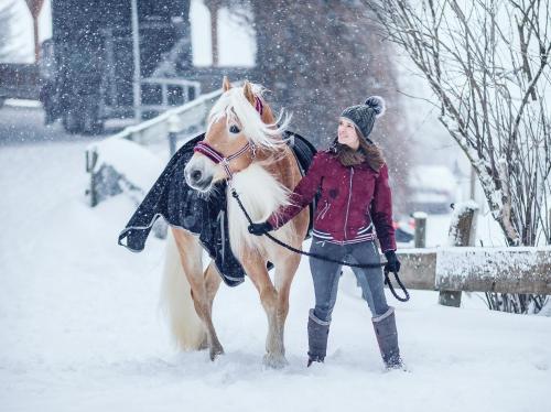 a woman standing next to a horse in the snow at Familienresort Ellmauhof - das echte All Inclusive in Saalbach Hinterglemm