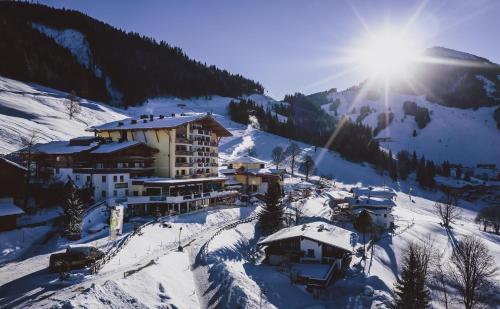 a building on a snow covered mountain in the sun at Familienresort Ellmauhof - das echte All Inclusive in Saalbach Hinterglemm