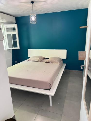 a bed in a room with a blue wall at Petite Maison Contemporaine in Rivière-Salée