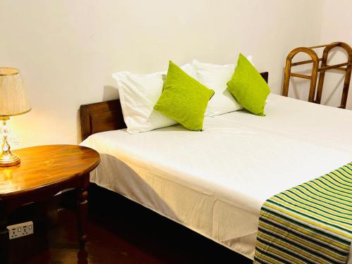 a bedroom with a bed with green pillows and a table at Rosewood Bungalow in Bandarawela