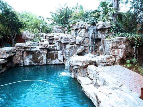 a swimming pool with a waterfall and a rock wall at Tudor Lodge Guest House in Johannesburg