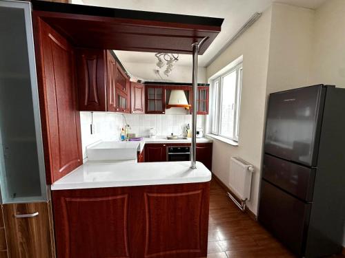 a kitchen with wooden cabinets and a black refrigerator at Cosy spacious 3 bedroom apartment in Ulaanbaatar