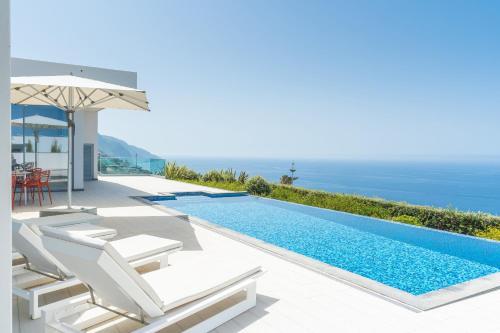a villa with a infinity pool and chairs and an umbrella at Villa Alegria by Atlantic Holiday in Calheta