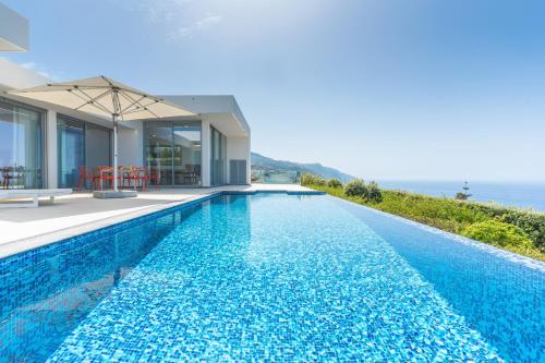 a swimming pool in front of a house with the ocean at Villa Alegria by Atlantic Holiday in Calheta