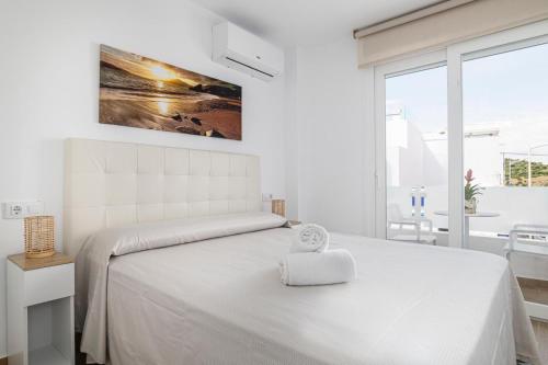 a white bedroom with a large white bed and a window at Apartamentos Almadraba in Zahara de los Atunes