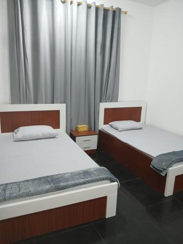two twin beds in a room with a curtain at Guest house sohar in Sohar