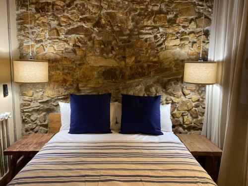 a bed with blue pillows in a room with a stone wall at Stone Rustic Beach apartment in Blanes
