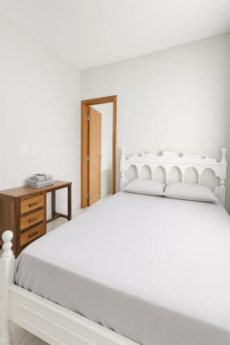 a white bedroom with a white bed and a wooden table at Apto próximo Ufu, Parque do Sabia, Madrecor in Uberlândia