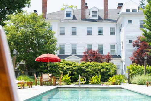a pool with a red umbrella and chairs and a house at The Red Lion Inn in Stockbridge
