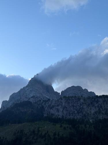 a cloud hovering over a mountain range with trees at Guesthouse Drinos Valbone in Valbonë